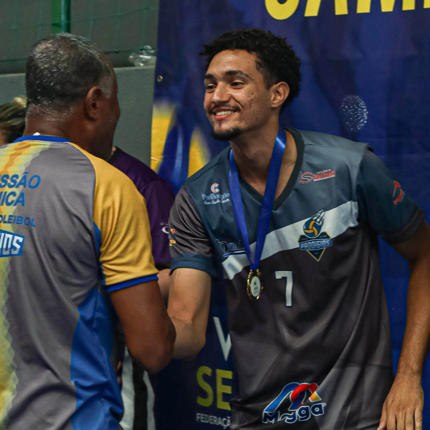 Atleta do Prodígios de medalha no peito, cumprimentando um membro da comissão técnica